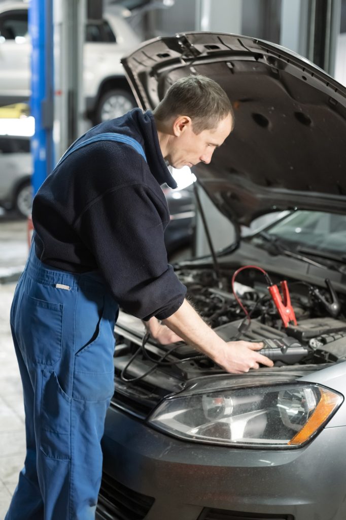 Mechanic examining car under the hood at the repair garage.